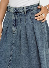 Jupe en denim bleu clair avec des plis, taille haute et poches avant. La ceinture comporte des passants de ceinture. La texture est lisse avec une finition légèrement décolorée.