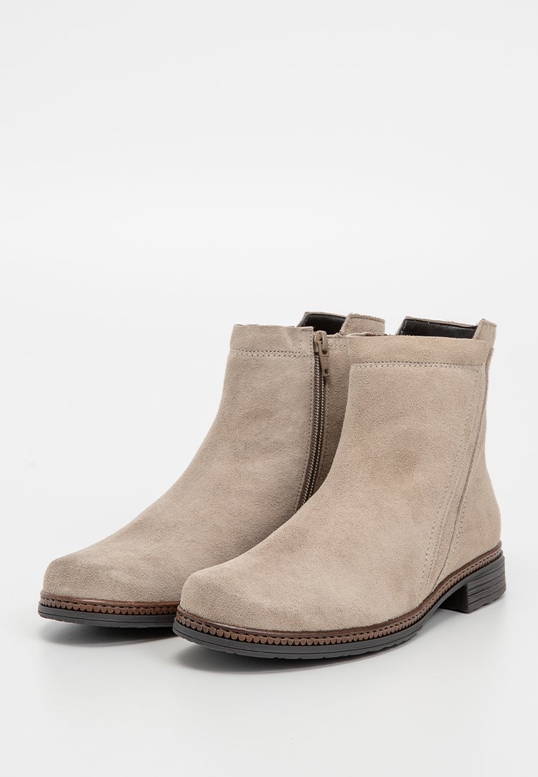 Beżowe zamszowe botki sięgające kostki z niskim, wypukłym obcasem, bocznym zamkiem błyskawicznym oraz dekoracyjnym przeszyciem wzdłuż podeszwy. Gładka, strukturalna powierzchnia.