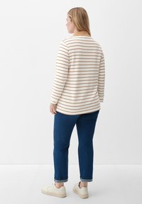 White long-sleeve shirt with thin horizontal beige stripes, paired with dark blue denim pants and casual beige sneakers. Back view.