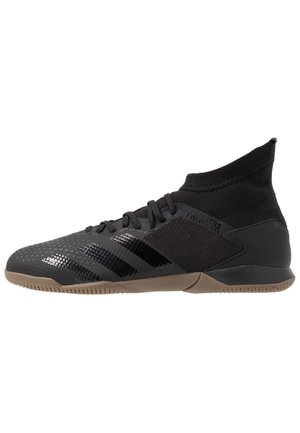 Schwarzer Hallenfußballschuh mit sockenähnlichem Knöchelkragen, strukturierter Obermaterial, drei glänzenden Streifen und hellbrauner Sohle.
