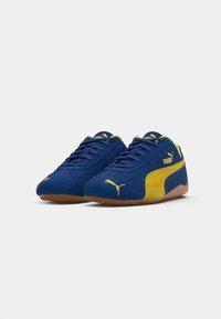 Blauwe suède sneakers met gele accenten en veters. Heeft een rubberen zool en een gele Puma-logo op de zijkant en de tong. Lichtgewicht ontwerp.