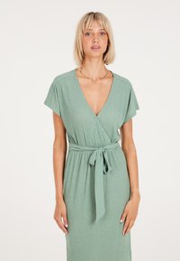 Vestido envolvente verde con mangas cortas, tejido texturizado, escote en V y detalle de cintura atada. Diseño simple y elegante.