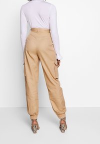 Beige cargobyxor med en avslappnad passform, elastiska muddar och sidofickor, tillsammans med en långärmad vit topp och mönstrade klackar.