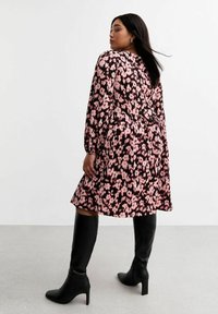 Blumenmuster-Kleid in Rosatönen und Schwarz, mit langen Ärmeln, einer taillierten Taille und einem knielangen Rock. Kombiniert mit schwarzen knielangen Stiefeln.