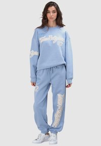Ensemble sweat-shirt et pantalon de jogging bleu clair avec marquages blancs et numéros, en coton, coupe décontractée, poignets et ourlets de cheville côtelés.