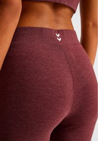 Leggings met hoge taille in een donkerbordeauxrode stof met een gladde textuur. Voorzien van drie witte chevrons nabij de tailleband en een strakke pasvorm.