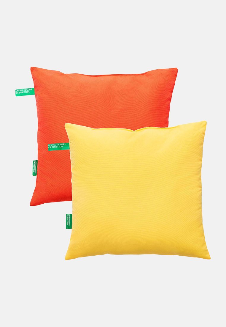 Deux oreillers carrés avec une surface texturée ; l'un est orange et l'autre est jaune. Chacun a une petite étiquette verte dans un coin.
