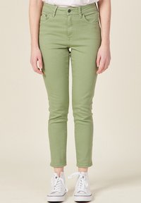 Jeans verdes de corte ajustado, material de algodón, diseño de cinco bolsillos y dobladillos enrollados; combinados con zapatillas altas blancas.