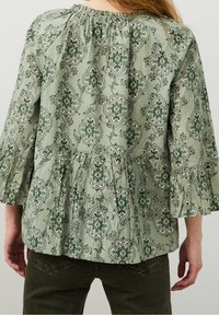 Grön mönstrad blus med en rynkad halsringning, utsvängda ärmar och en peplumslutning, med blommiga och geometriska mönster i mörkare nyanser.