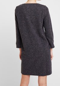 Robe tricotée foncée à manches longues, présentant un tissu texturé avec des éclats multicolores, et une silhouette à coupe droite.