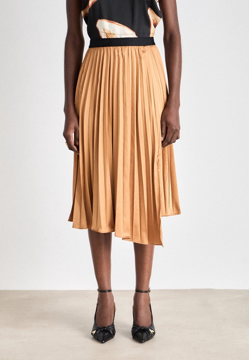 Falda plisada de longitud media en tela de color naranja claro con una textura suave, que cuenta con una cinturilla elástica. Combinada con tacones negros de punta afilada.