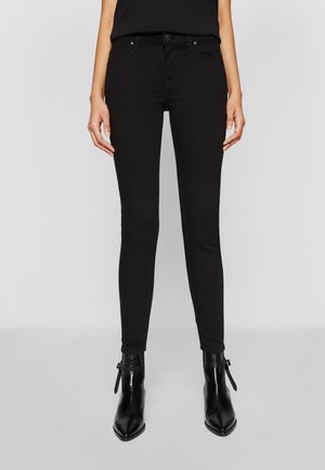 Jeans skinnys negros de cintura alta, con cinco bolsillos y costuras en contraste, combinados con botines negros de punta afilada.