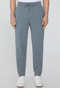 Jasnoniebieskie spodnie dresowe z elastycznym paskiem i sznurkiem do regulacji, z wypustkami na mankietach i gładką fakturą, w połączeniu z białymi trampkami.