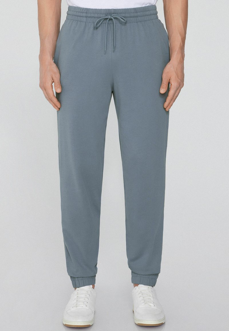 Jasnoniebieskie spodnie dresowe z elastycznym paskiem i sznurkiem do regulacji, z wypustkami na mankietach i gładką fakturą, w połączeniu z białymi trampkami.
