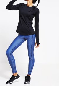 Svart långärmad träningsskjorta, blå mönstrade leggings och svarta träningsskor. Leggings har en texturerad design och kontrasterande sömmar.