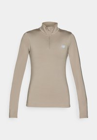 Haut de sport à manches longues beige avec un col montant et une fermeture éclair quart. Il présente un petit logo bleu clair sur le côté gauche de la poitrine. Texture lisse.