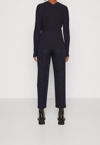 Maglione a coste blu navy con maniche lunghe e scollo a V, abbinato a pantaloni dritti blu scuro e stivaletti neri con tacco.