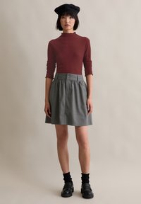 Bordó bordázott hosszú ujjú felső, szürke csíkos szoknya redőkkel, fekete beret, fekete loaferek, és térdig érő fekete zoknik.