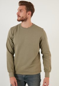 Sudadera de manga larga verde oliva con cuello redondo y puños acanalados, que presenta una tela texturizada y un diseño minimalista.