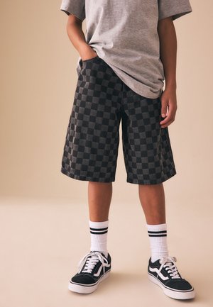 Barn iført grå T-shirt, sorte og grå ternede shorts, hvide sokker med sorte striber og sorte sneakers med hvide snørebånd.