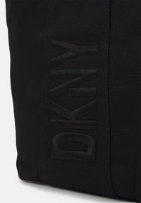 Borsa a spalla nera in canvas con logo DKNY in rilievo, tessuto testurizzato, forma rettangolare e cuciture robuste sui lati.