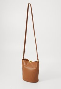Sac en cuir marron en forme de seau avec un fond plat, une bandoulière réglable et un fermoir circulaire en or en haut, présentant une texture lisse et un design minimaliste.