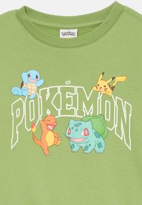 T-shirt verde in cotone con quattro Pokémon cartoon: Squirtle, Charmander, Bulbasaur e Pikachu, con testo "POKÉMON" in bianco.