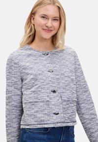 Wollen blend geknipte jas in een gestructureerd grijs en wit patroon. Bevat vier zwarte knopen en twee voorzakken. Brede ronde halslijn.