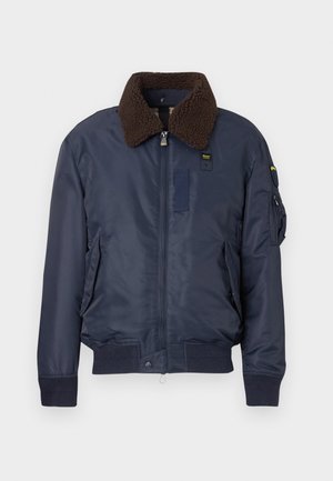 Giacca bombarolo navy con colletto in pelliccia sintetica marrone, chiusura con zip, tasche laterali e toppe in tessuto. Polsini e orlo a coste completano il design.