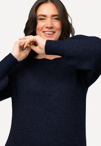 Pull en tricot bleu marine avec une texture côtelée, un col rond large et des manches longues légèrement bouffantes.
