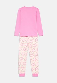 Top roz cu mâneci lungi, cu umeri volanți, asociat cu pantaloni de pijama crem cu motive de stele roz și manșete roz.