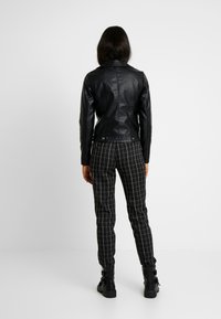 Sort læderjakke med tætsiddende design og ribbet detalje på ærmerne, kombineret med sorte og hvide ternede tilspidsede bukser og sorte støvler.