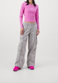 Fitted långärmad rosa topp med vit logotyp, parat med lösa grå cargobyxor med sidofickor och elastisk midja. Klara rosa sneakers.