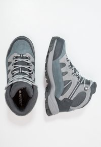 Botas de senderismo grises con parte superior de ante y malla, suela de goma, ojales reforzados y acentos texturizados. Cuenta con un collar acolchado para mayor comodidad.