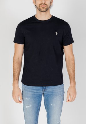Camiseta de algodón azul marino con escote redondo y mangas cortas; presenta un pequeño logo bordado en el pecho; combinada con jeans de mezclilla claros y desgastados.