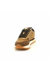 Bruine en tan sneaker met een gestructureerde suede neus, zwarte veters, gouden accenten en een gepatterde hak op een witte rubberen zool.