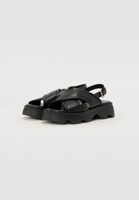 Sorte lær sandaler med en tyk, struktureret sål, der har krydsende stropper og en justerbar spænde på siden.