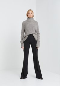 Grau gerippter Strickpullover mit Rollkragen und langen Ärmeln, kombiniert mit schwarzen maßgeschneiderten Hosen in gerader Beinform.