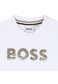 Λευκό βαμβακερό t-shirt με μεγάλη, υφασμένη ασημί γραφιστική "BOSS" στο μπροστινό μέρος. Στρογγυλή λαιμόκοψη με λεπτομέρεια κουμπιού στον ώμο.