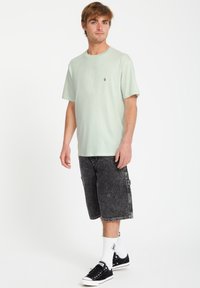 Lys grøn bomulds t-shirt med korte ærmer og et lille logo, parret med mørk vaskede denimshorts og sorte sneakers med hvide sokker.
