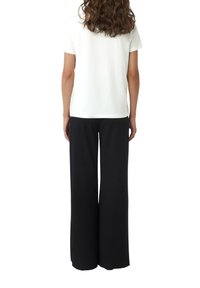 Witte kortemouw T-shirt met een ronde hals, gecombineerd met vloerlange zwarte wijde broek. Beide items hebben een gladde textuur.