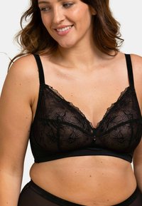 Bralette en dentelle noire avec broderie florale, bretelles ajustables et fermeture à agrafes. Un tissu doux et transparent ajoute de la texture et des détails.
