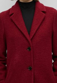 Rood wollen blend jas met een gestructureerde afwerking, voorzien van een notch revers, drie knopen en twee zijzakken.