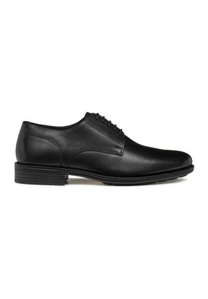 Zapato de vestir de cuero negro con punta redondeada, textura suave y detalle con cordones. Cuenta con un tacón bajo y apilado y suturas sutiles.