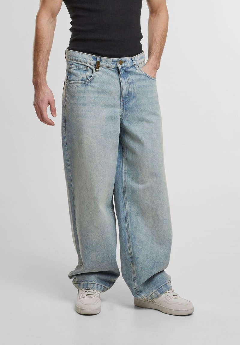 Pantaloni in denim oversize blu chiaro con design a gamba dritta, dotati di cinque tasche e dettagli di cucitura visibili. Indossati con una canotta nera.