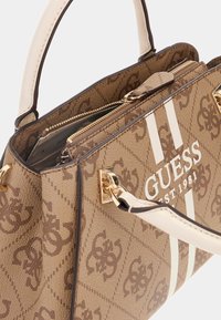 Sac à main marron à motifs avec des accents beige, des doubles poignées et des finitions en or. Il dispose d'une poche zippée et d'un logo de marque imprimé à l'avant.