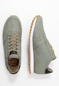 Vaaleanvihreät lenkkarit, joissa on teksturoitu, kivetty nahkapinta, vaaleat nauhat, mustat yksityiskohdat, valkoinen välipohja ja kumipohja.