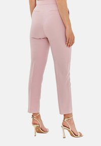 Jasnoróżowe dopasowane spodnie o wąskim kroju, z tylkimi kieszeniami, w zestawie ze złotymi sandałami na wysokim obcasie z paskami. Gładka tekstura materiału.