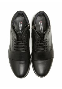 Chaussures habillées en cuir noir avec lacets et fermetures éclair latérales, cols rembourrés, et inscription "Redskins" à l'intérieur sur fond blanc.