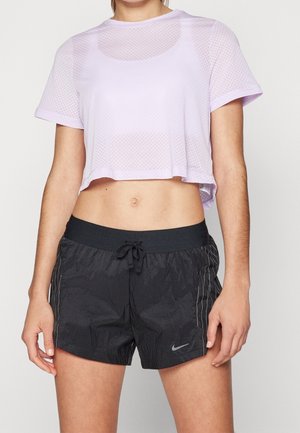 Kvinde iført en lyse lilla netkort T-shirt og sorte Nike-shorts med snor i taljen og reflekterende striber.